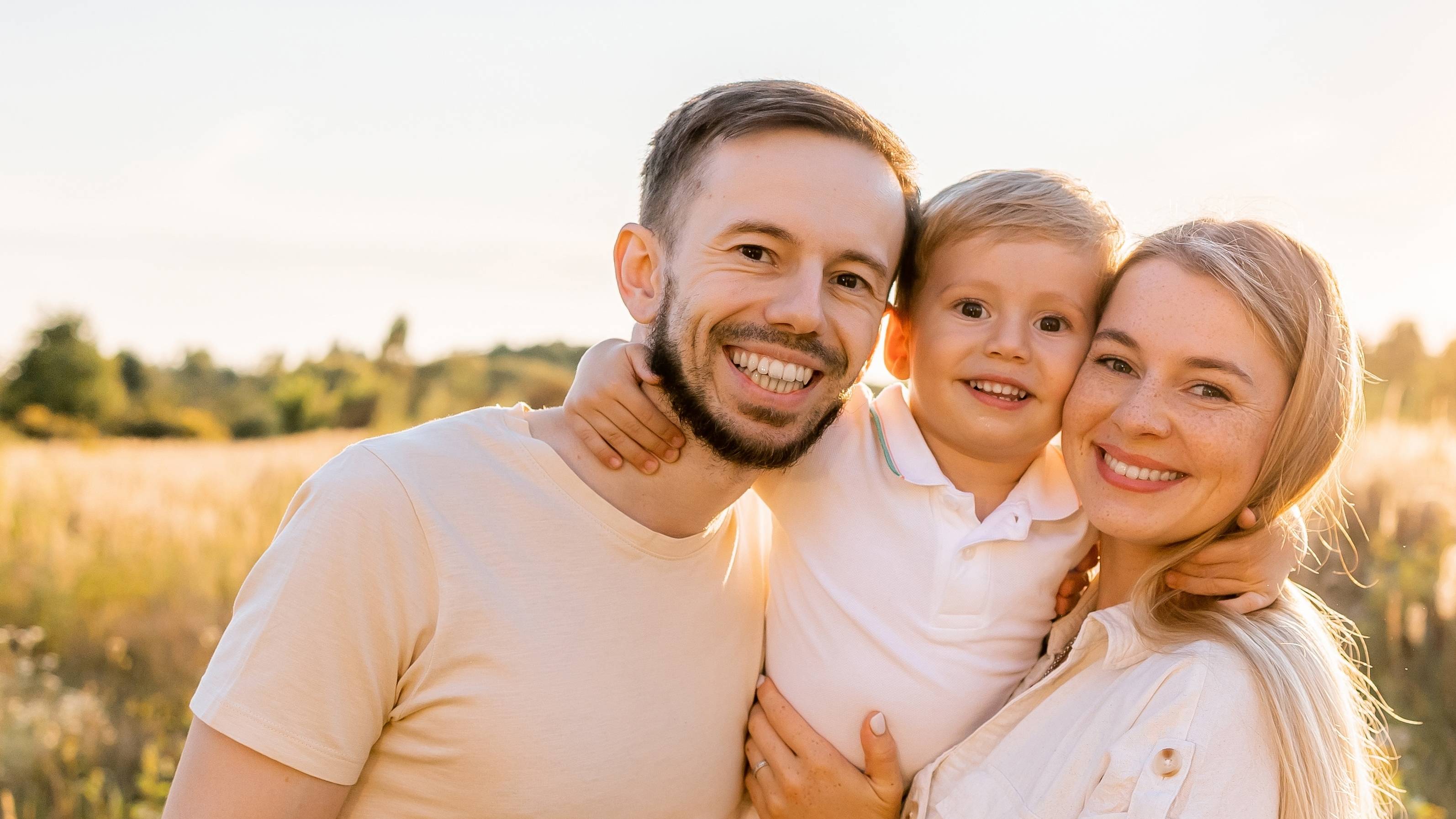 Family of three smiling together in a sunlit field