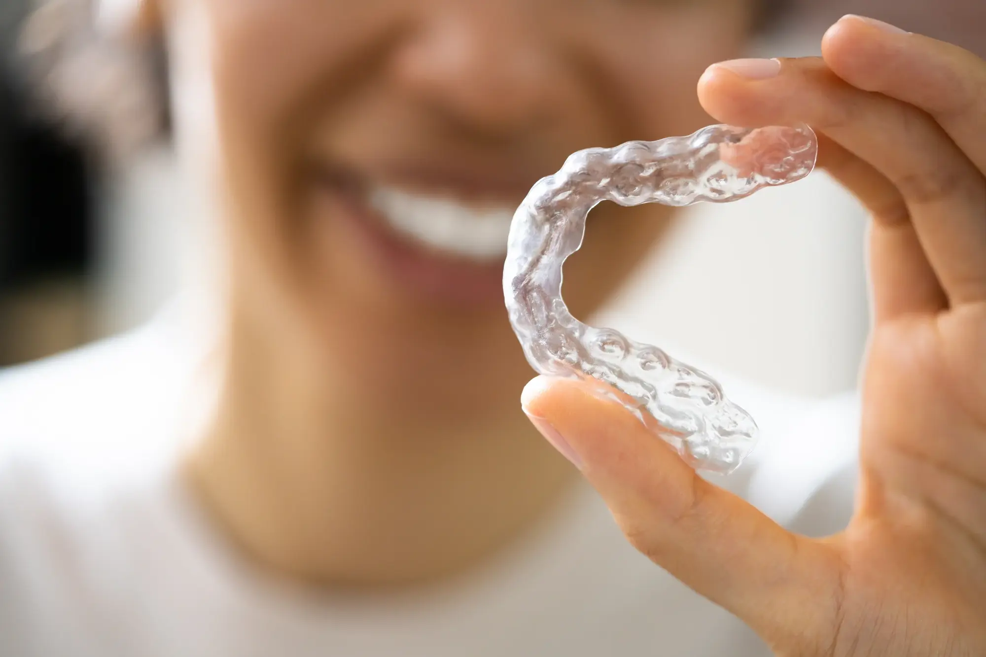 Patient holding a clear aligner tray up to her smile